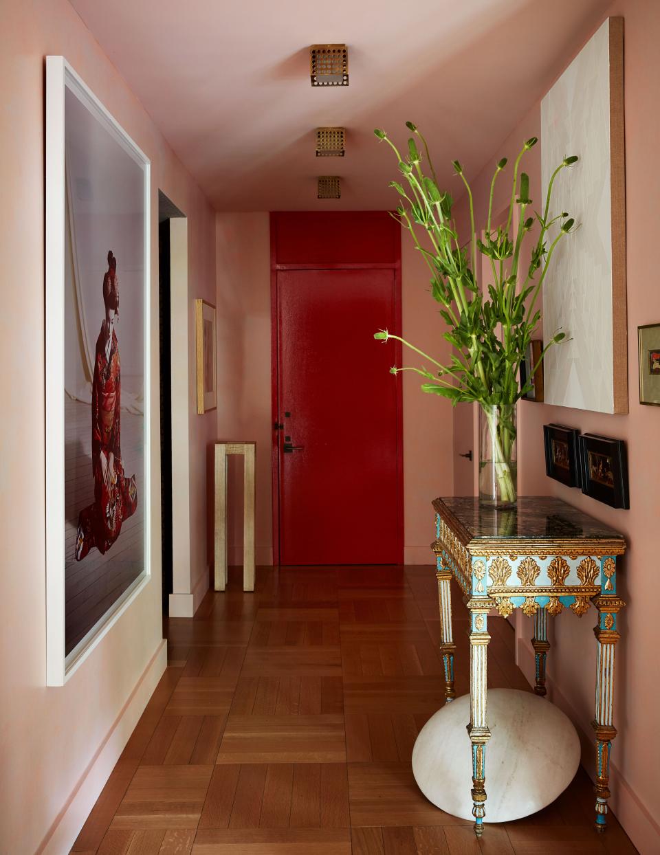 Benjamin Moore shades of pink and red warm the entrance hall, where a Laurie Simmons photograph faces a circa 1780 piedmontese table; white painting by Andrew Kuo.