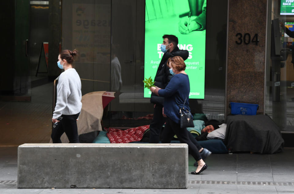 Three people wearing face masks walk past a homeless person sleeping on George Street in the CBD on August 09, 2020 in Sydney, Australia. (Photo by James D. Morgan/Getty Images)