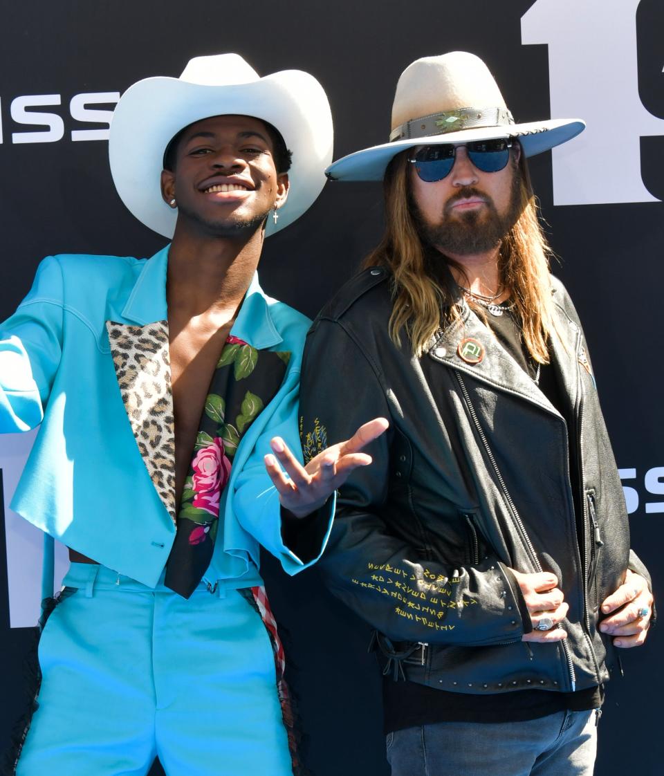 Lil Nas X in a boldly patterned suit and cowboy hat poses with Billy Ray Cyrus in a leather jacket and wide-brim hat at the BET Awards