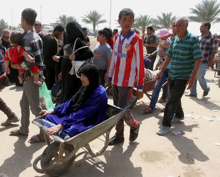 A woman is transported in a wheelbarrow as displaced Sunni people, who fled the violence in the city of Ramadi, arrive at the outskirts of Baghdad, April 18, 2015. REUTERS/Stringer