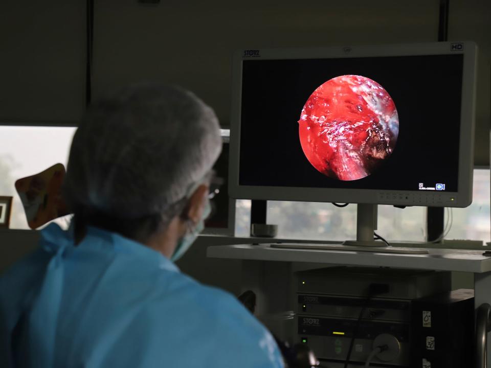 doctor in scrubs and hairnet looks at large screen with red circular image on it