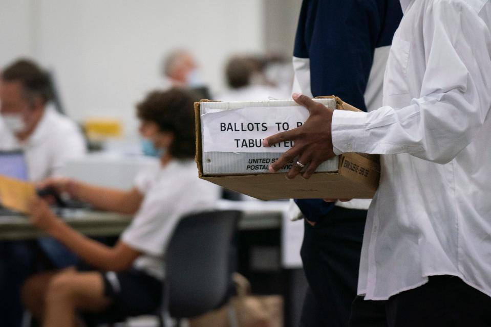 A supervisor carries a box of absentee ballots to be counted inside Hall E of Huntington Place in downtown Detroit on Tuesday, Aug. 2, 2022.