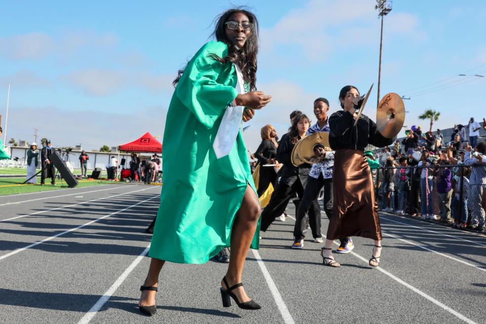 A girl dances on a track as other people play instruments behind her.