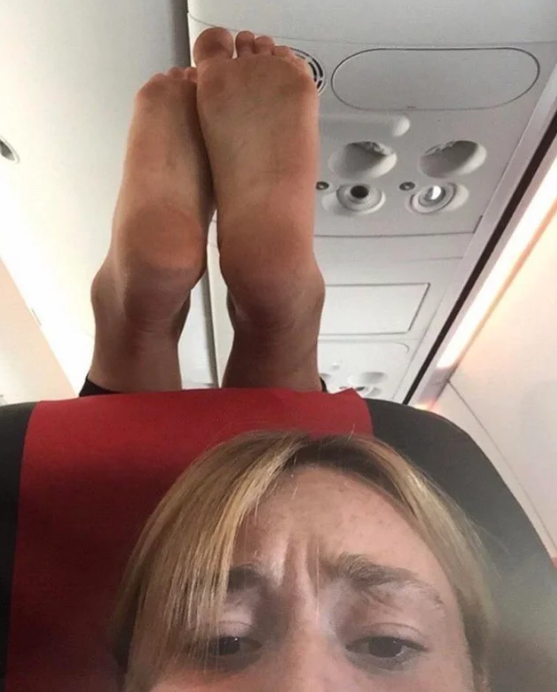 The woman is pictured frowning as the other passenger's feet dangle just above her head.Source: Reddit