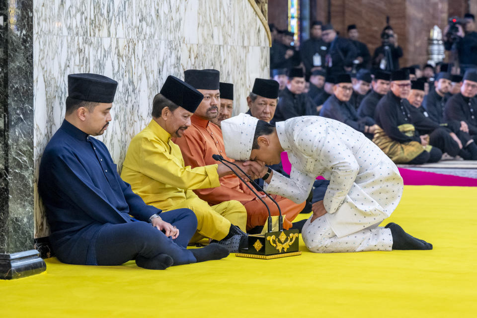 This handout picture taken by Brunei's Information Department on January 11, 2024 and released on January 12, 2024 shows Brunei's Prince Abdul Mateen, right, touching his forehead on his father's hand, Brunei's Sultan Haji Hassanal Bolkiah, second from left, after his solemnization at Sultan Omar Ali Saifuddien Mosque in Bandar Seri Begawan, Brunei. (Brunei's Information Department via AP)