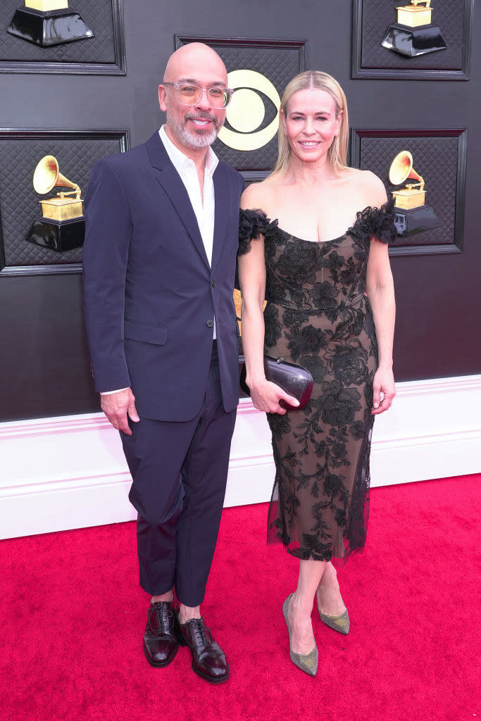 Jo in a suit and Chelsea in a calf-length, off-the-shoulder lacy dress