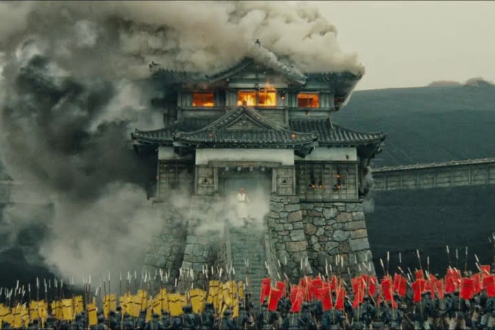 Two armies stand in front of a burning building in Ran.