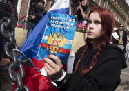 A woman handcuffs herself to a fence while holding a Constitution of the Russian Federation, during a rally supporting Khabarovsk region's governor Sergei Furgal in St.Petersburg, Russia, Saturday, Aug. 1, 2020. Thousands of demonstrators rallied Saturday in the Russian Far East city of Khabarovsk to protest the arrest of the regional governor, continuing a three-week wave of opposition that has challenged the Kremlin. (AP Photo/Dmitri Lovetsky)