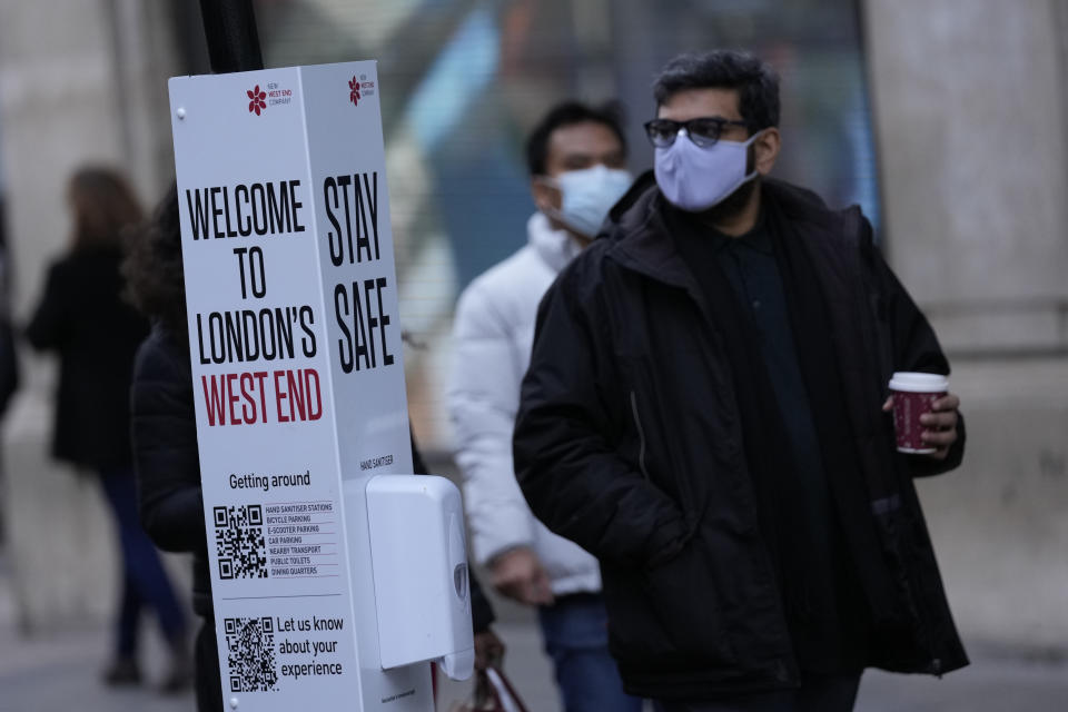 Bus passengers wait at a bus stop next to a Stay Safe sign which encourages social distancing and the wearing of masks to curb the spread of COVID-19, in London, Tuesday, Nov. 30, 2021. The emergence of the new COVID-19 omicron variant and the world's desperate and likely futile attempts to keep it at bay are reminders of what scientists have warned for months: The coronavirus will thrive as long as vast parts of the world lack vaccines.(AP Photo/Alastair Grant)