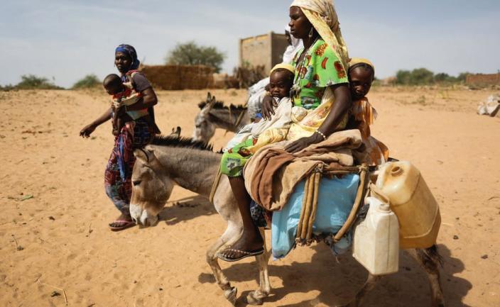 Displaced women and children in Darfur carry their belongings, helped by donkeys