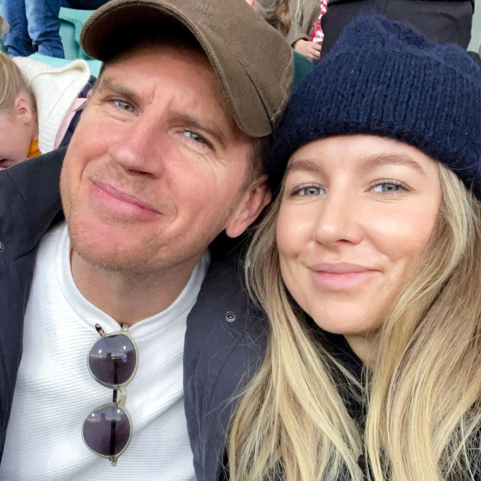 Selfie of Sam Mac wearing a brown baseball cap, white shirt and black glasses hanging from the collar, next to Rebecca James, wearing a navy blue beanie and her blonde hair out. 