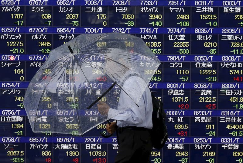 A man holding an umbrella walks in front of an electronic stock quotation board outside a brokerage in Tokyo September 8, 2015. REUTERS/Issei Kato