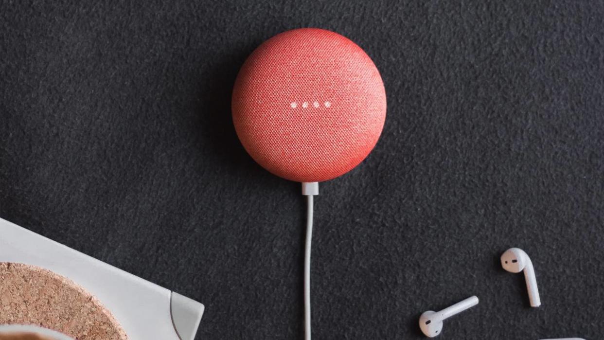  A red Google Nest Mini sitting on a table next to AirPods. 