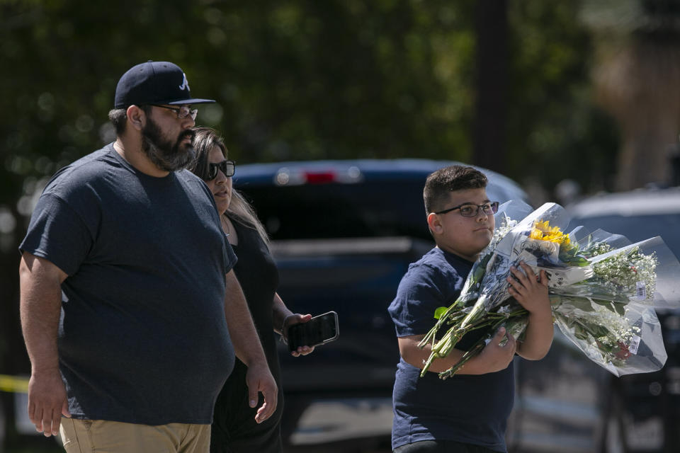 Visitors carry flowers to the memorial created outside Robb Elementary School in Uvalde, Texas, Thursday, May 26, 2022. On Tuesday, a gunman entered the school and at least 19 students and two educators were killed. (Josie Norris/The San Antonio Express-News via AP)