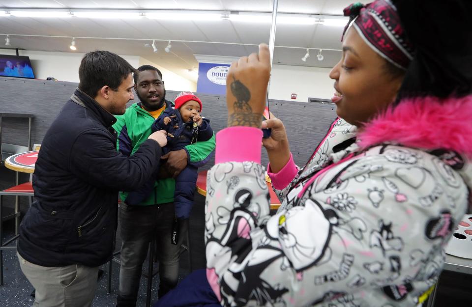 Akron Mayor Shammas Malik, left, tries to get the attention of Javiontae Bitting Jr. as he and his dad, Javiontae Sr., pose for Lanijah Hamilton, right, as she takes a photo during Tumble Together Thursday at Super Clean Laundromat on Thursday.