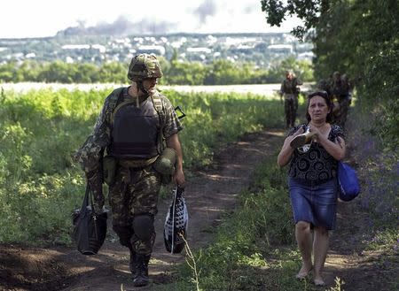 Ukrainian army soldier from battalion "Aydar" helps a local resident as she leaves the village of Metalist near the eastern Ukrainian city of Luhansk July 11, 2014. REUTERS/Viktor Gurniak