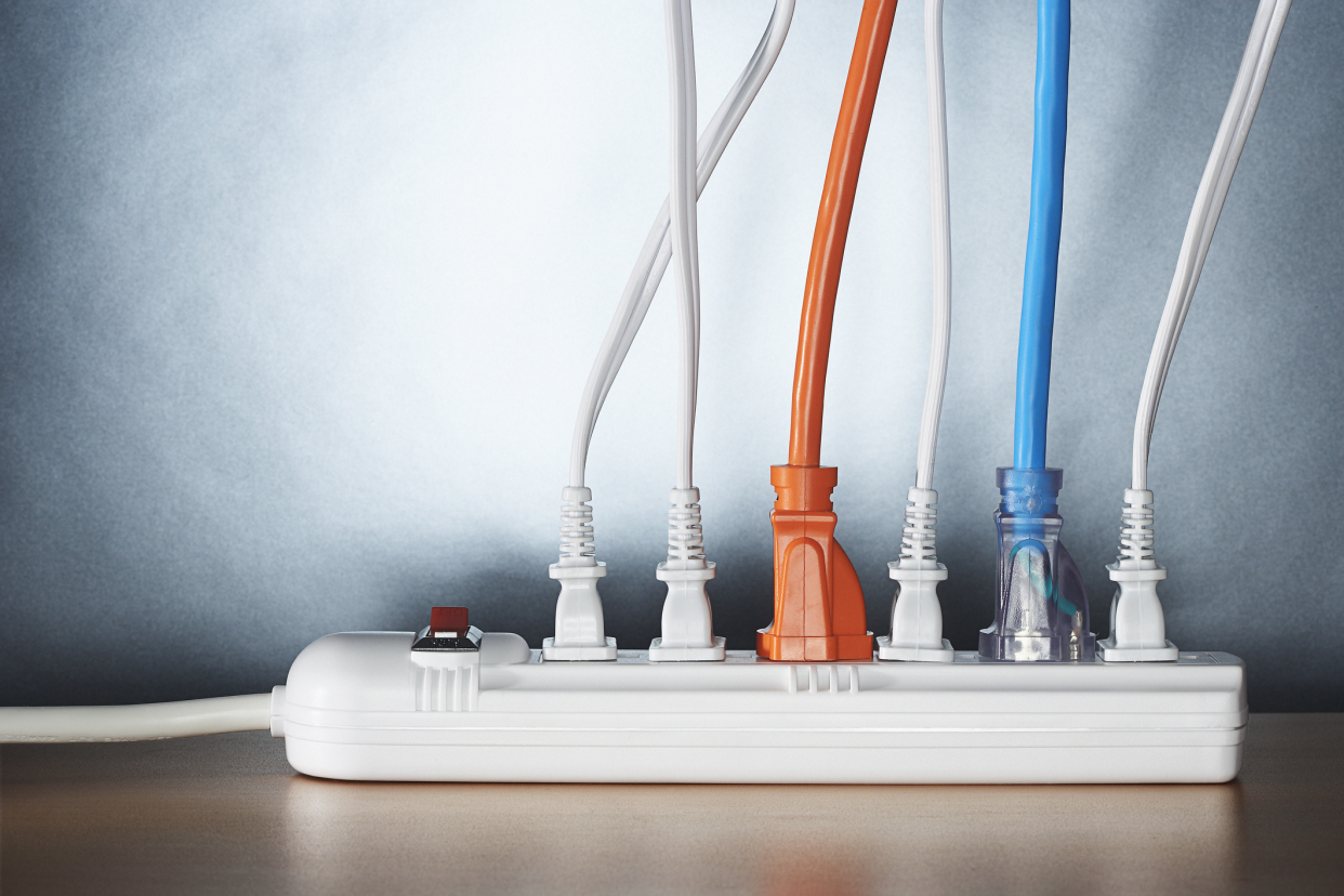 Focus on six colorful cords in a white surge protector, on a wooden floor with a grey gradient wall background