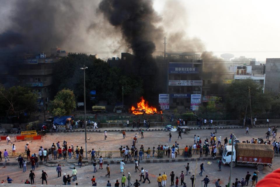 People watch as a car burns during clashes in Delhi (AP)