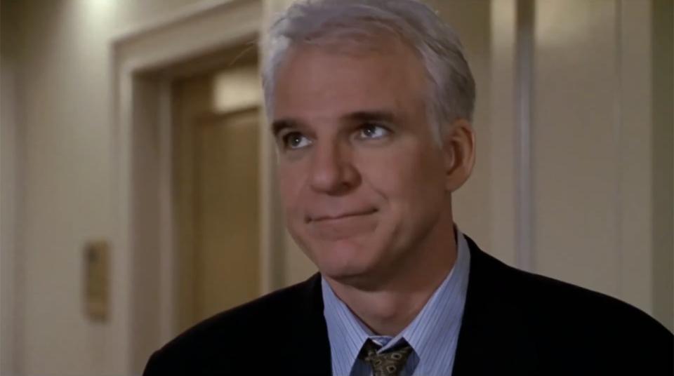 Steve Martin in a suit and tie, indoors, looking slightly to the side with a thoughtful expression