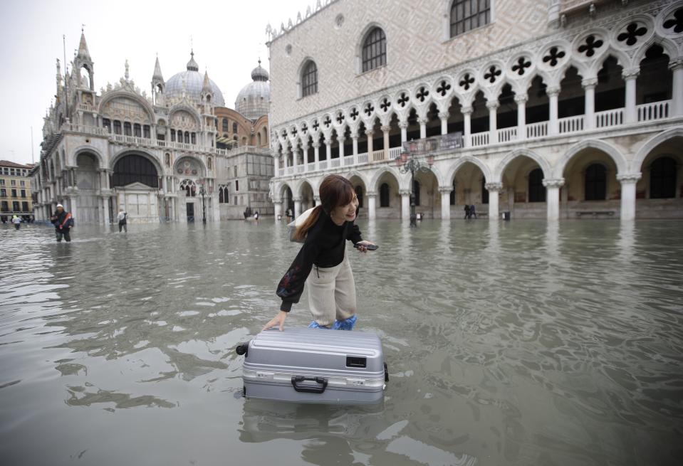 A tourist pushes her floating luggage in a flooded St. Mark's Square, in Venice, Wednesday, Nov. 13, 2019. The high-water mark hit 187 centimeters (74 inches) late Tuesday, Nov. 12, 2019, meaning more than 85% of the city was flooded. The highest level ever recorded was 194 centimeters (76 inches) during infamous flooding in 1966. (AP Photo/Luca Bruno)