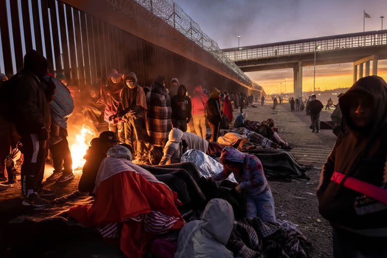 Inmigrantes se calientan con el fuego después de pasar la noche junto a la valla fronteriza entre Estados Unidos y México, en el Paso