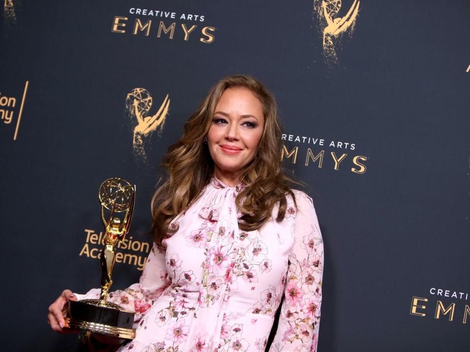 leah remini holding a trophy in front of a creative emmys backdrop