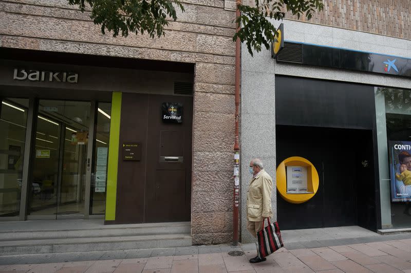 A man walks past branches of Bankia and Caixabank in Madrid