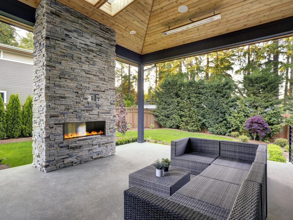 Outdoor patio surrounded by greenery with a gray seating area and gray stone fireplace