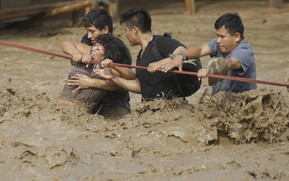 En esta imagen del 17 de marzo de 2017, varias personas atrapadas por las inundaciones se aferran a una cuerda para vadear las aguas crecidas hasta un lugar seguro en Lima, Perú. Las intensas lluvias y deslaves de los últimos tres días han sembrado el caso en la nación andina y tomado por sorpresa a los vecinos de Lima, una ciudad desértica de 10 millones de personas donde casi nunca llueve. (AP Foto/Martín Mejía)