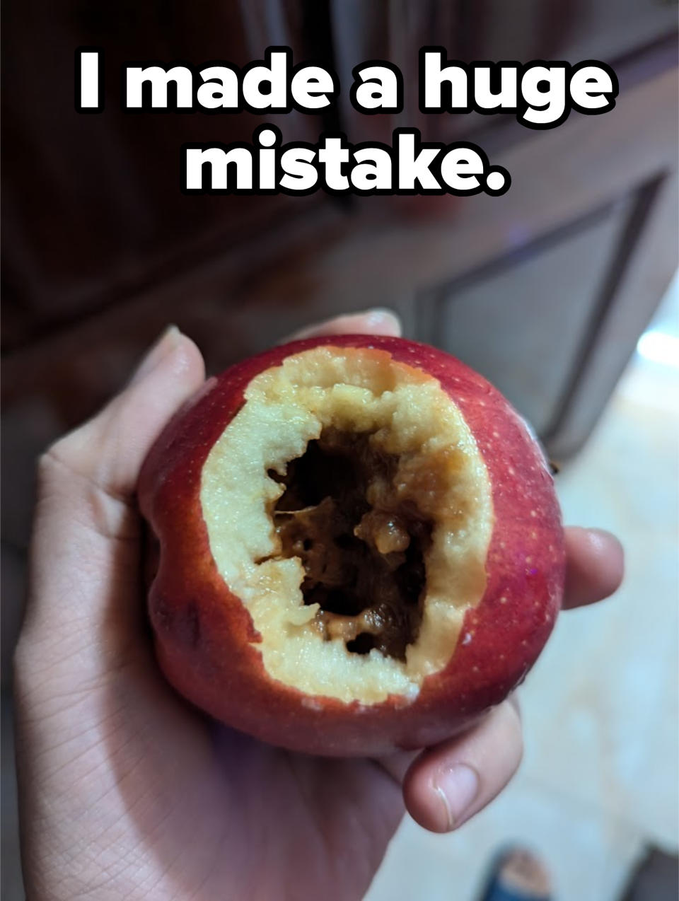 A hand holding a bitten apple with its core exposed and brown, rotten areas visible