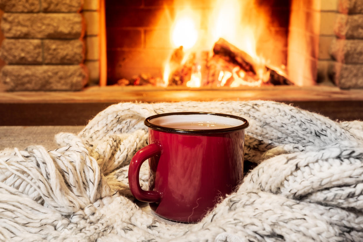 A red mug nestled within a blanket in front of a roaring fire. 