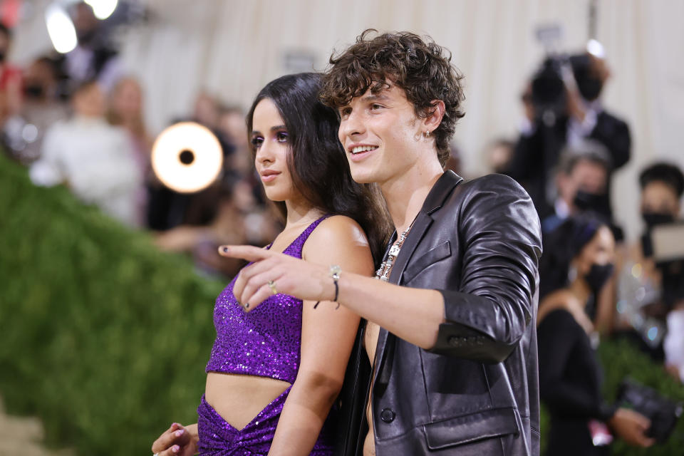 Camila Cabello in a sparkly crop-top and skirt, links arms with Shawn Mendes, who's wearing an open leather jacket on the red carpet as they pose on the red carpet