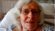 Annette Smith lying on a bed, with white hair and glasses