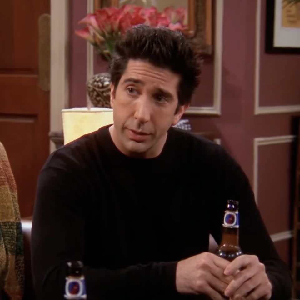 Paul Rudd and David Schwimmer sit on a couch, talking, while holding beer bottles in a living room setting