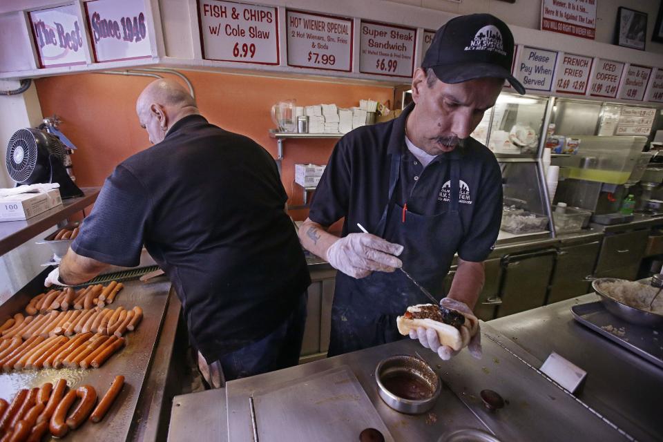 In this Monday, March 3, 2014 photo, manager Jimmy Saccoccio, left, works the grill as Sal O'Brien preps a hot wiener "all the way" at Olneyville New York System of Providence in Providence, R.I. The James Beard Foundation named the Rhode Island restaurant one of five "American Classics". (AP Photo/Stephan Savoia)