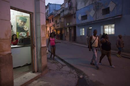 People walk on a street and past a state-run milk store with a photograph of Cuba's former President Fidel Castro in downtown Havana January 9, 2015. REUTERS/Alexandre Meneghini