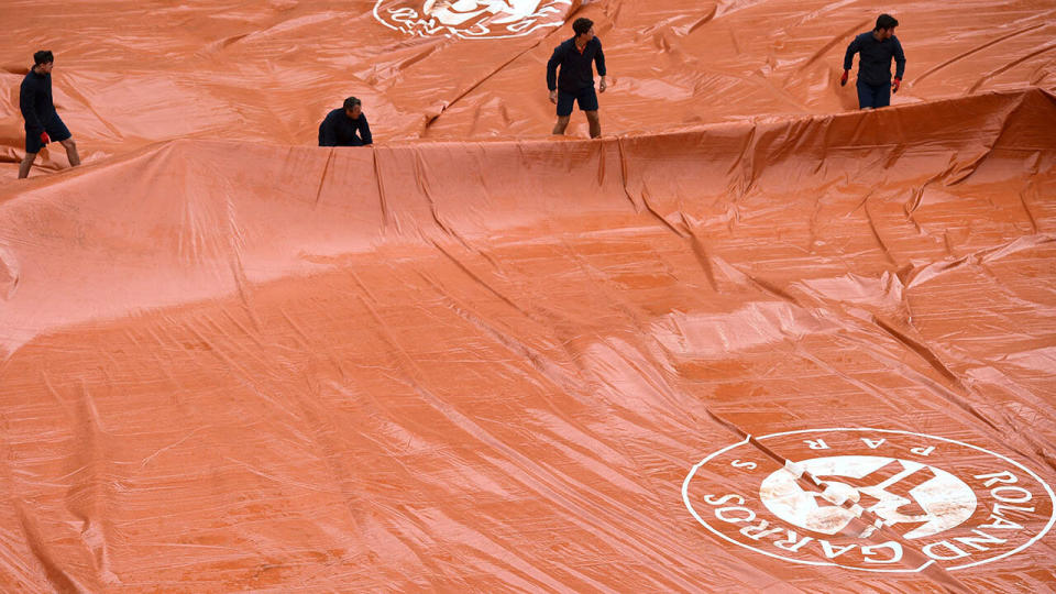 Groundstaff members pull covers across the court surface as rain falls. (Photo by MARTIN BUREAU/AFP/Getty Images)