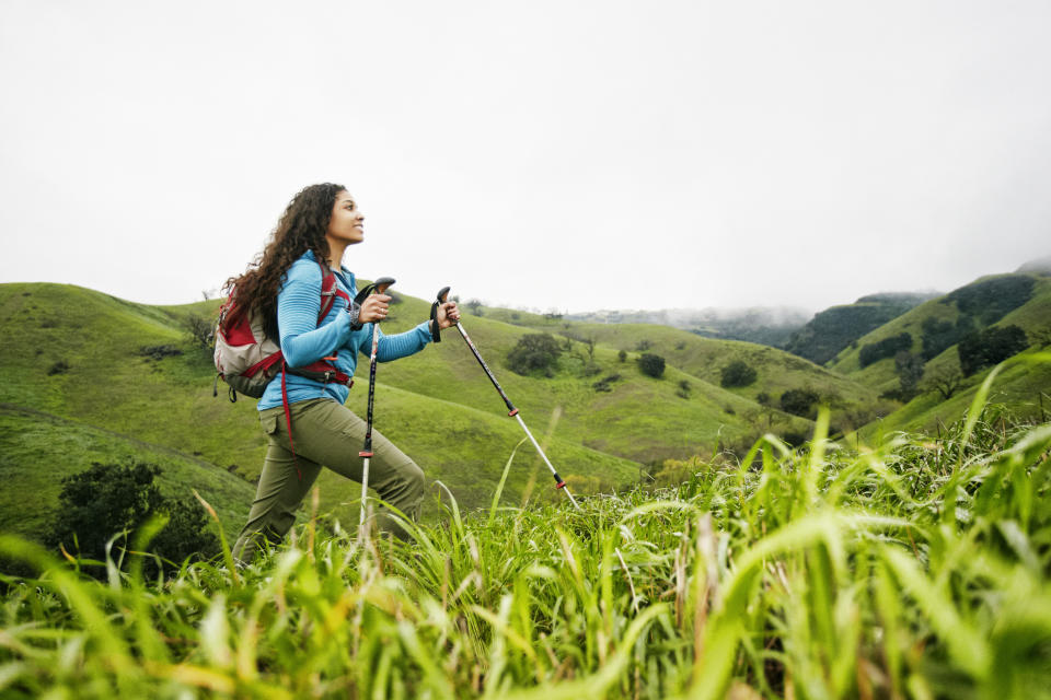 Woman hiking with poles on grassy hillside, focusing on the terrain ahead