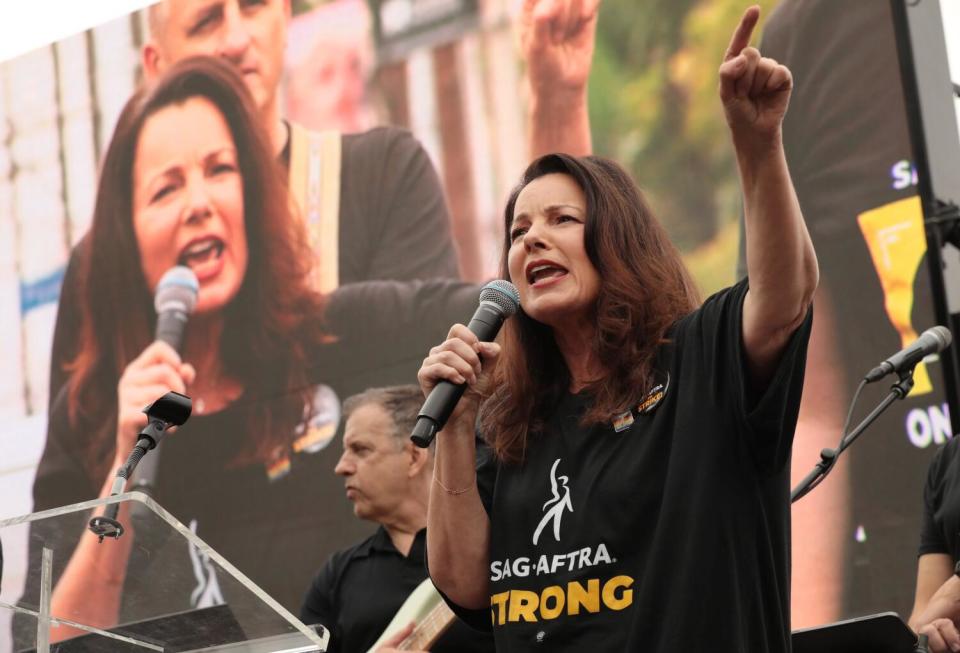 SAG-AFTRA President Fran Drescher speaks into a mic, with her image on a screen behind her.