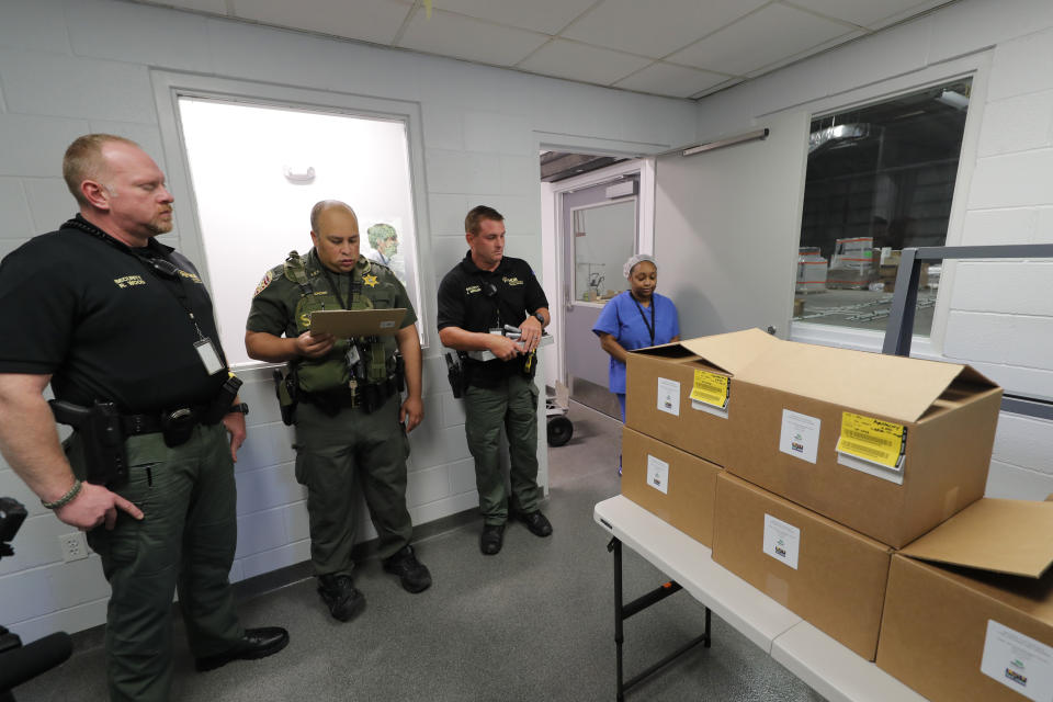 Shira Betts, an employee of GB Sciences Louisiana, readies the first ever boxes of legal medical marijuana in the state, as an East baton Rouge Sheriff deputy and two private security personnel stand by to protect the transport, in Baton Rouge, La., Tuesday, Aug. 6, 2019. (AP Photo/Gerald Herbert)