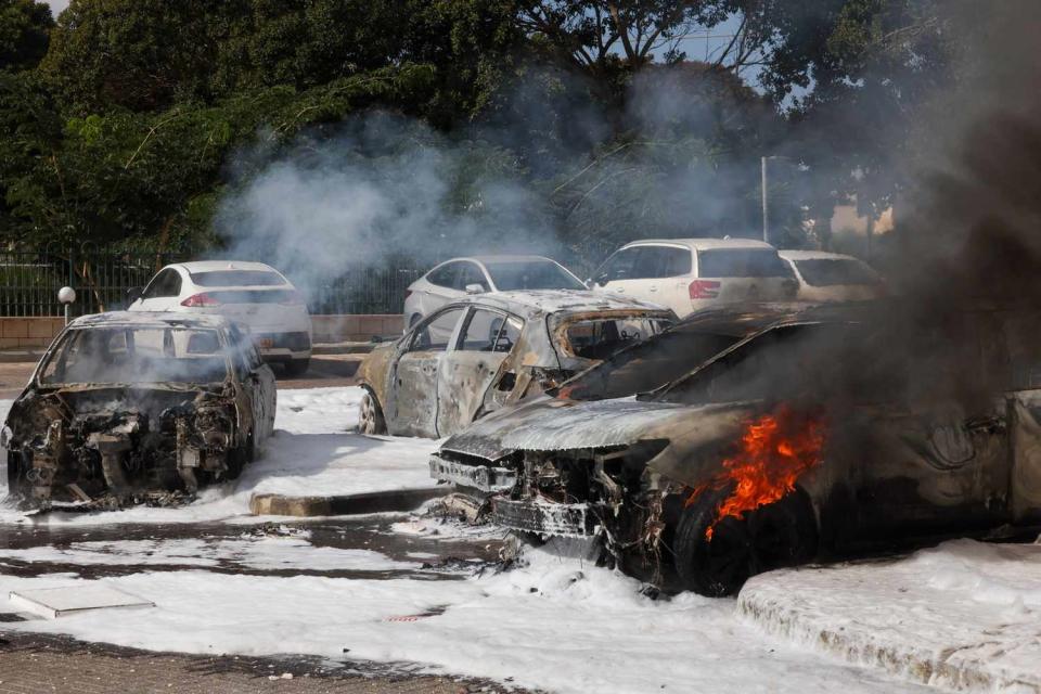 <p>AHMAD GHARABLI/AFP via Getty </p> Cars are seen on fire following a rocket attack from the Gaza Strip in Ashkelon, southern Israel, on Oct. 7, 2023