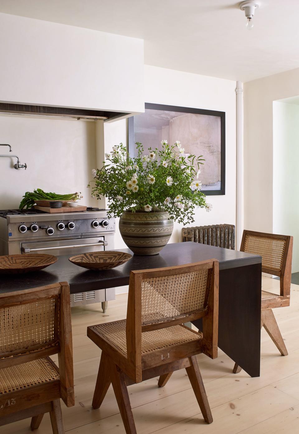 A long stone table with a steel frame, designed by Tedhams, anchors the open kitchen on the garden level. The teak and cane dining chairs are part of Pierre Jeanneret’s Chandigarh series, designed in the '50s for a project in India led by his cousin, Le Corbusier. The ceramic vase is a midcentury piece by Arthur Andersen, purchased at Maison Gerard.