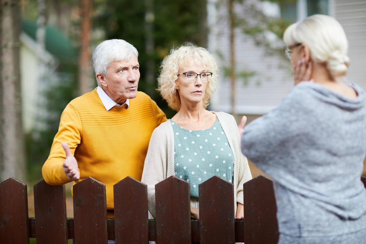 Irritated senior couple discussing trouble with their neighbour behind wooden fence