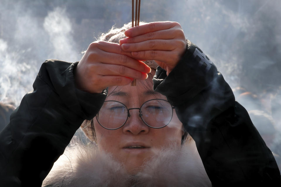 A woman holding incense sticks offers prayers on the first day of the New Year at Yonghegong Lama Temple in Beijing, Wednesday, Jan. 1, 2020. New Year's Eve isn't celebrated widely in mainland China, where the lunar New Year is a more important holiday. But countdown events were held in major cities, and some of the faithful headed to Buddhist temples for bell-ringing and prayers. (AP Photo/Andy Wong)