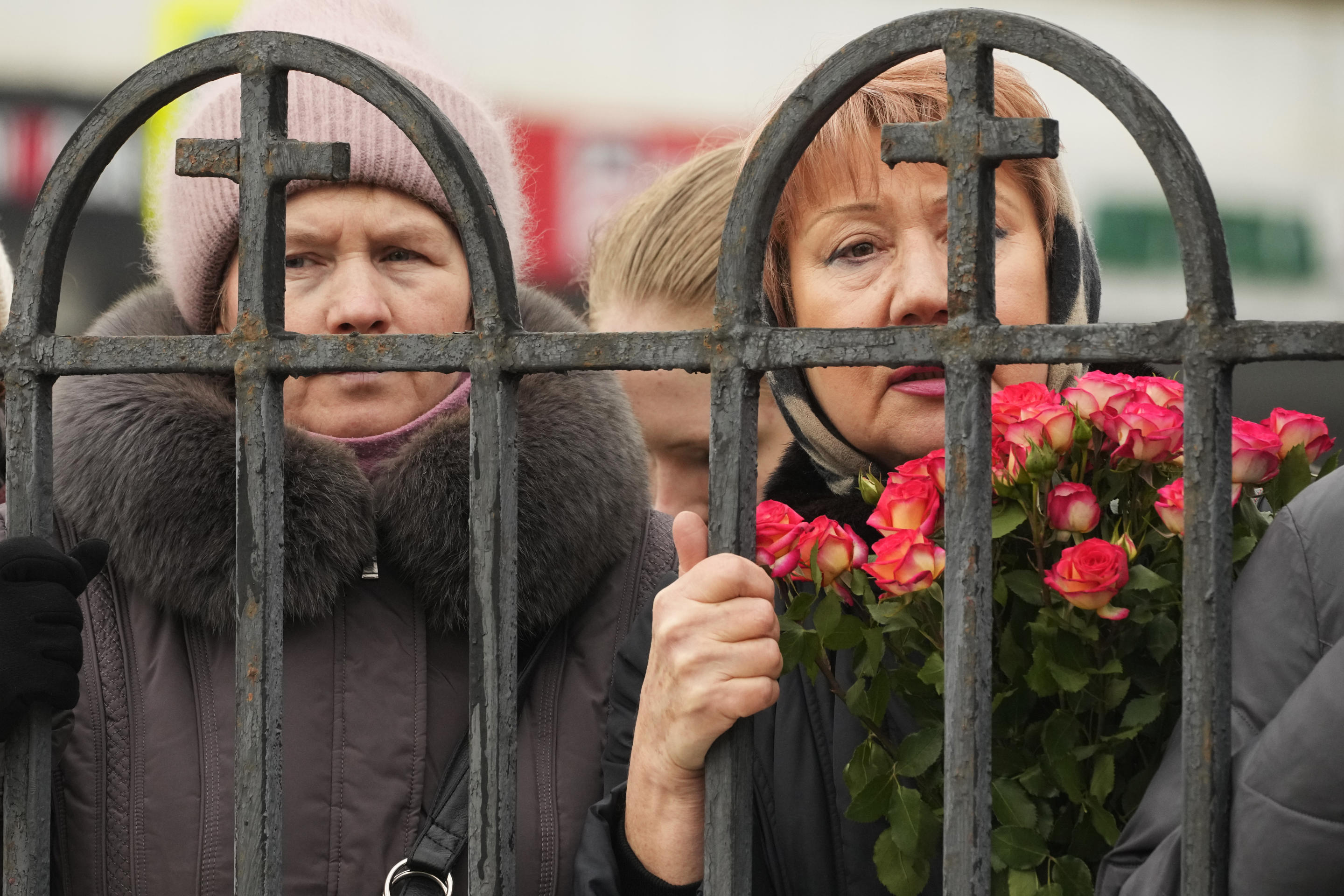 Several women, one holding a bouquet of roses, look through the metal bars of a fence outside the church where Navalny’s funeral was being held.