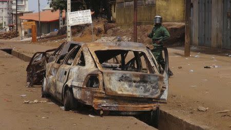 A security officer walks next to a burnt-out car in Conakry, Guinea, May 7, 2015. REUTERS/Saliou Samb