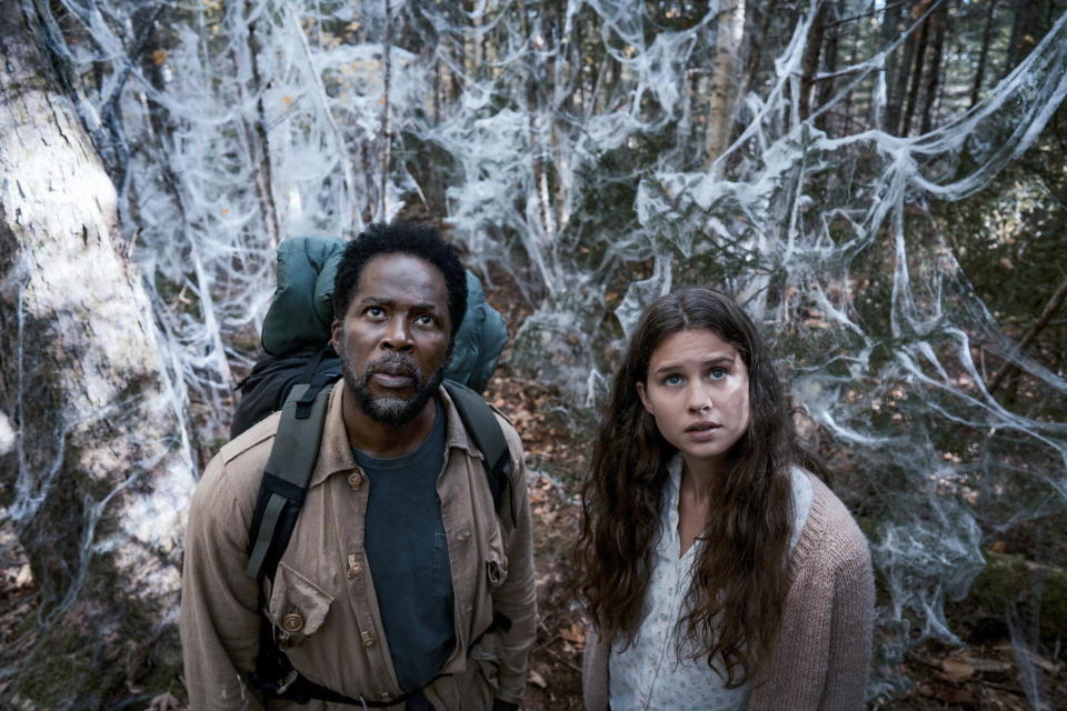 Two backpackers stare up at a strange thing in a cobweb-covered forest