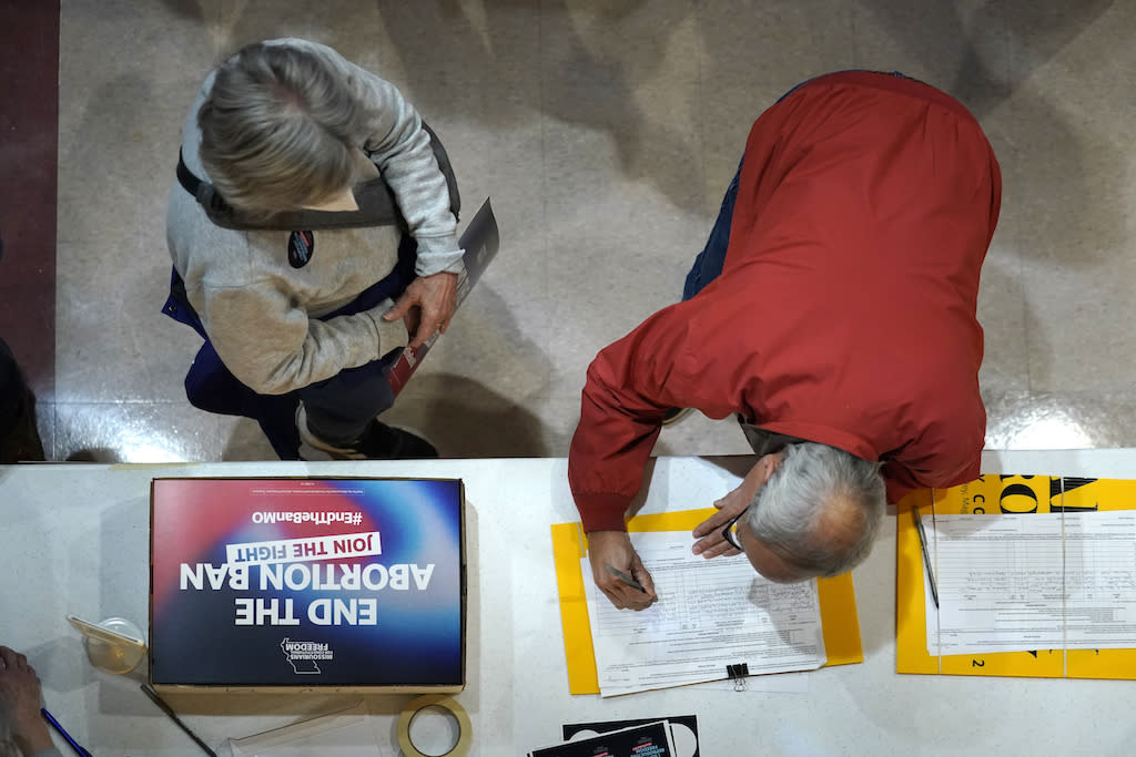 A top-down view man leaning over a table and signing a petition as a woman looks on.
