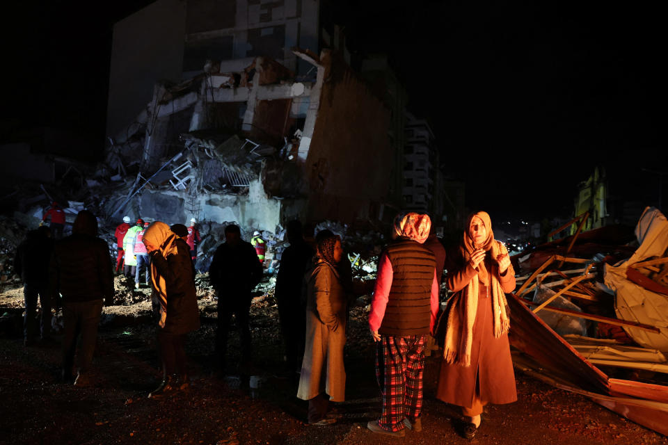 People look at a collapsed building near a bonfire following an earthquake in İskenderun, Turkey.