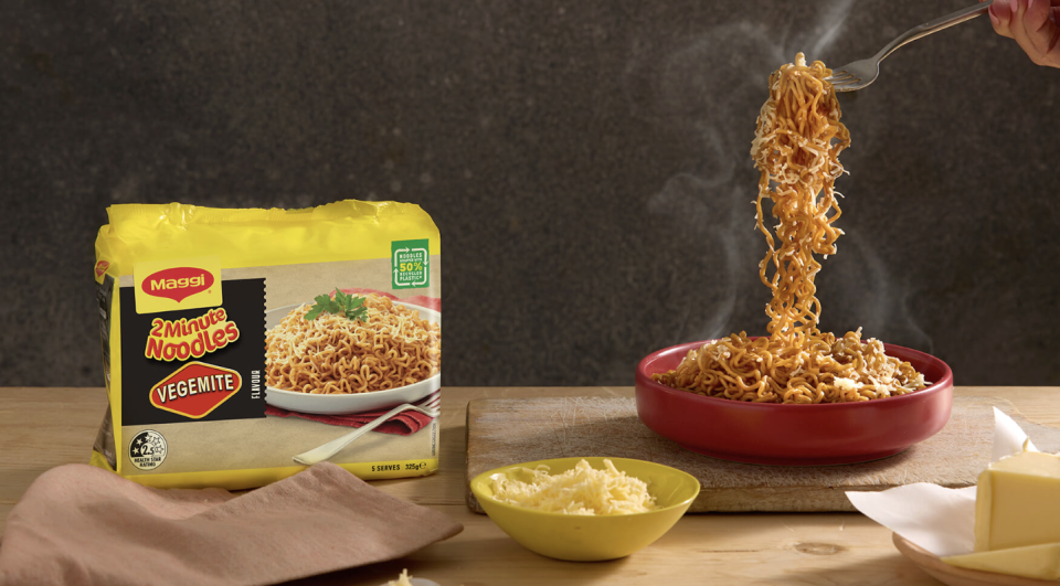 The four-pack of Maggi 2-minute Vegemite Noodles next to a bowl of the cooked noodles and some butter and cheese.